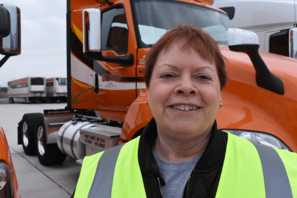 A happy female Osborn driver smiles in front of her orange Osborn day cab